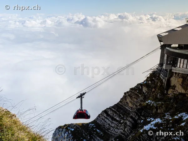 Rote Luftseilbahn vor der Bergstation des Pilatus über einer dichten Wolkendecke