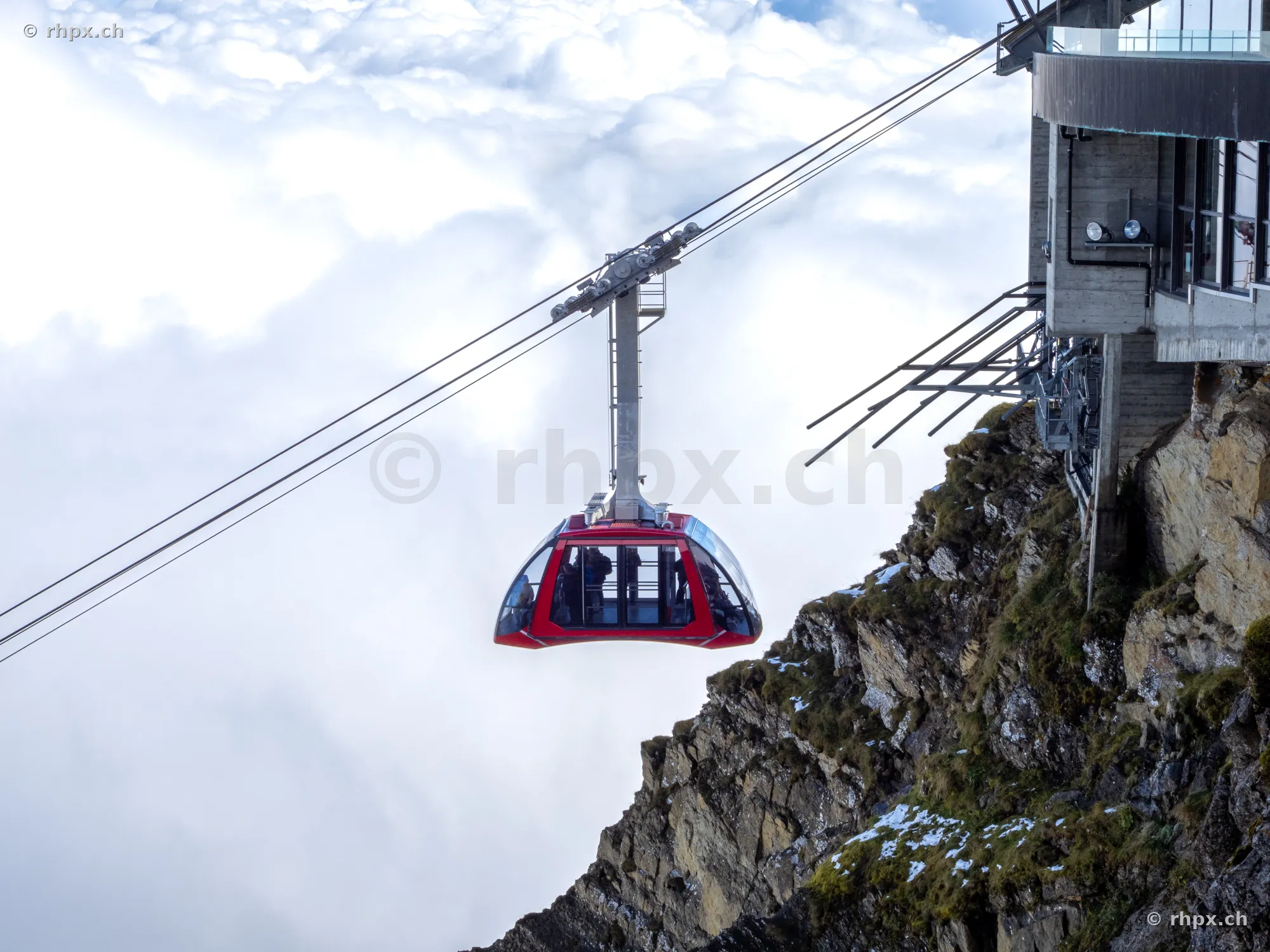 Red cable car in front of a rock face and a dense cloud cover at Mount Pilatus