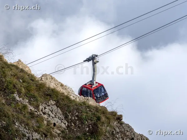 Red aerial cable car ascending Pilatus mountain over rocky terrain