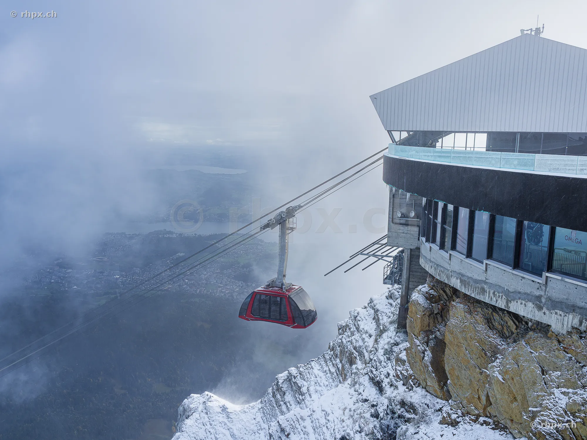 Red aerial cable car in front of the snowy Pilatus summit in the clouds