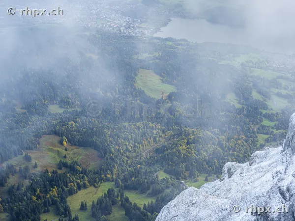 View from the snow-covered rocks of Mount Pilatus looking down on the wooded landscape below with lake and fog patches