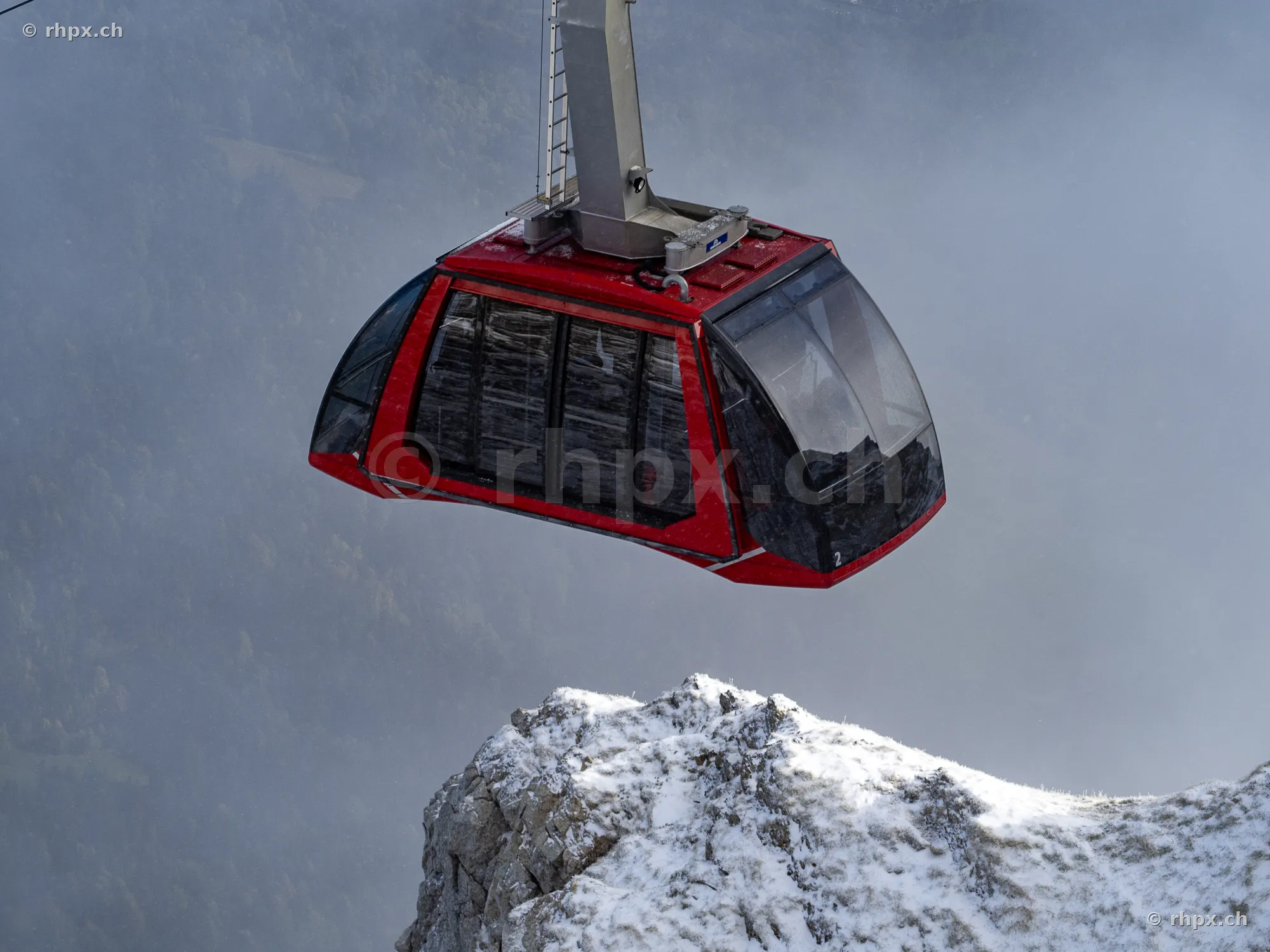 Red cable car of the Pilatus mountain railways over a snow-covered rock formation in fog