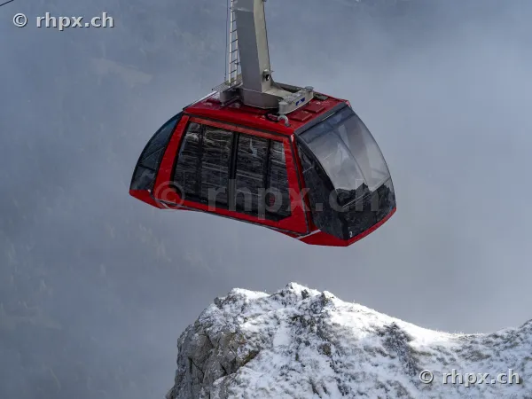 Rote Gondel der Pilatus-Bahnen über einer schneebedeckten Felsformation im Nebel