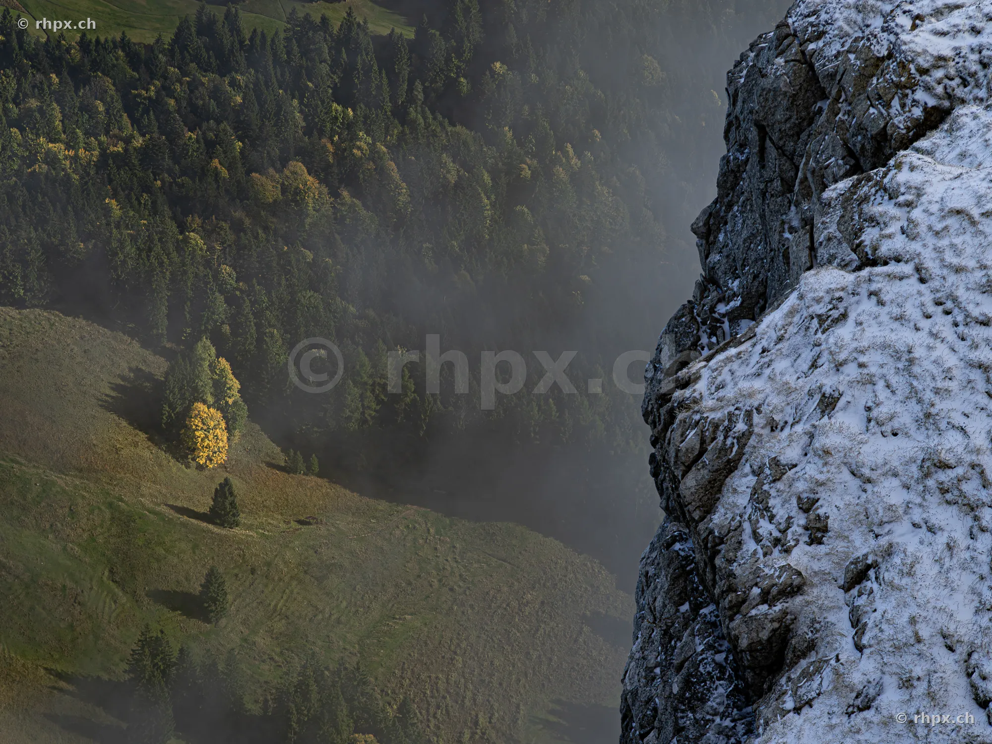 Steile, schneebedeckte Felswand am Pilatus mit Blick auf nebelverhangene Wälder