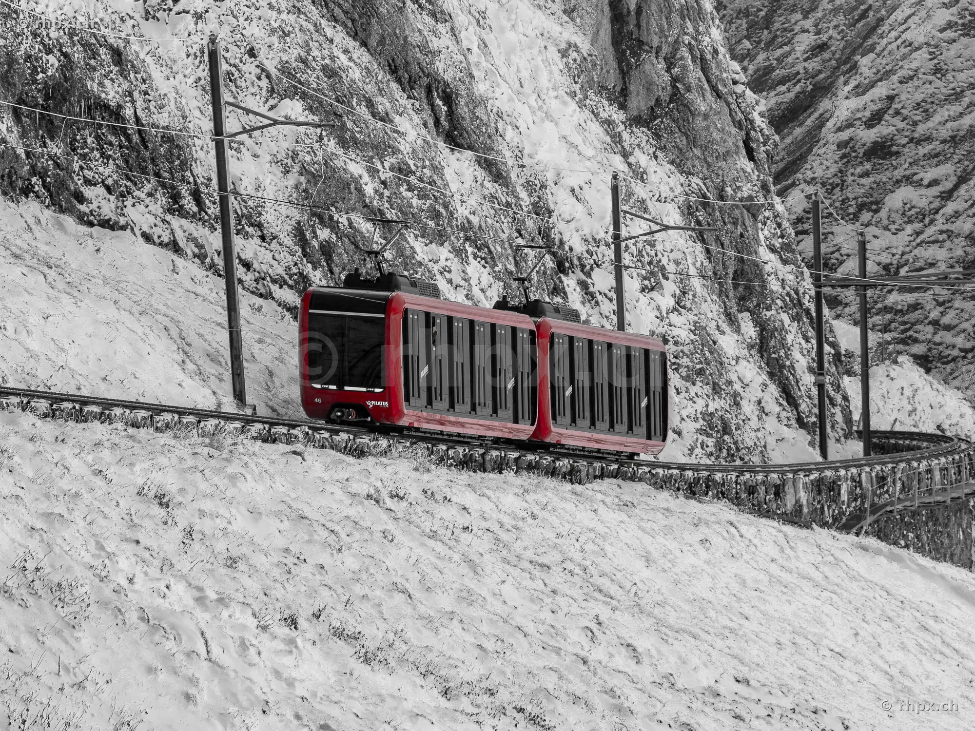 The red cogwheel train travels on a steep track through snowy rocky terrain on Mount Pilatus.