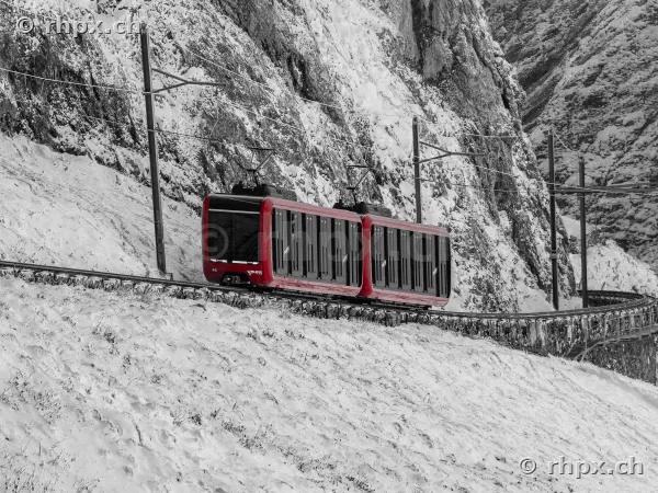 Die rote Zahnradbahn fährt auf steiler Strecke durch verschneites Felsgelände am Pilatus.