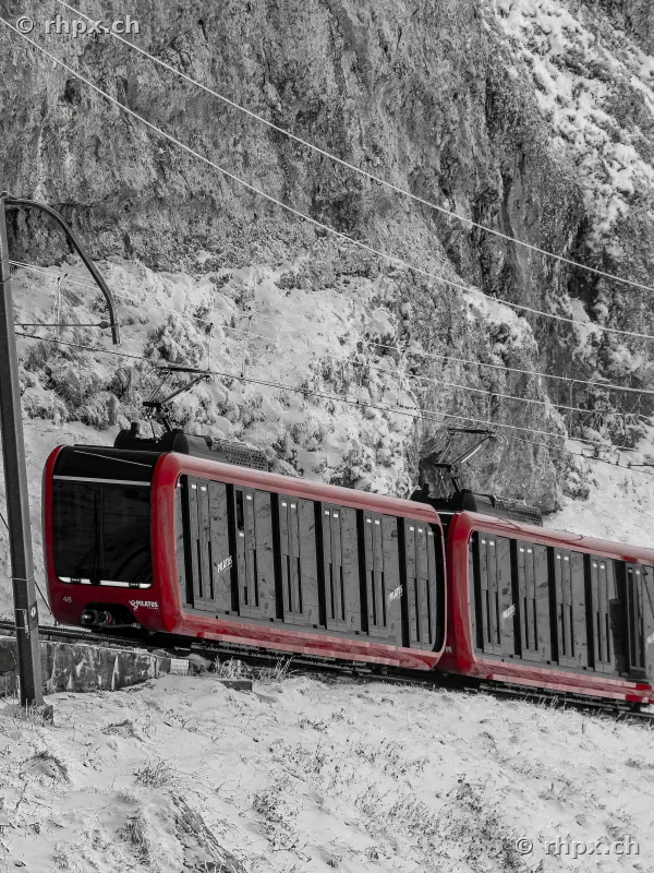 Roter Triebwagen der neuen Pilatusbahn auf steiler Strecke vor schneebedeckter Felswand