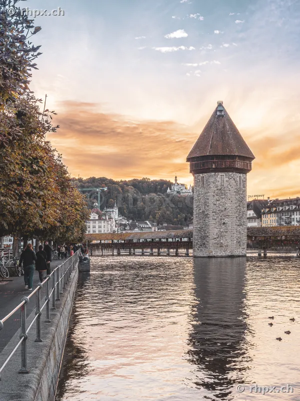 Water tower and Chapel Bridge in Lucerne at sunset seen from the riverbank.