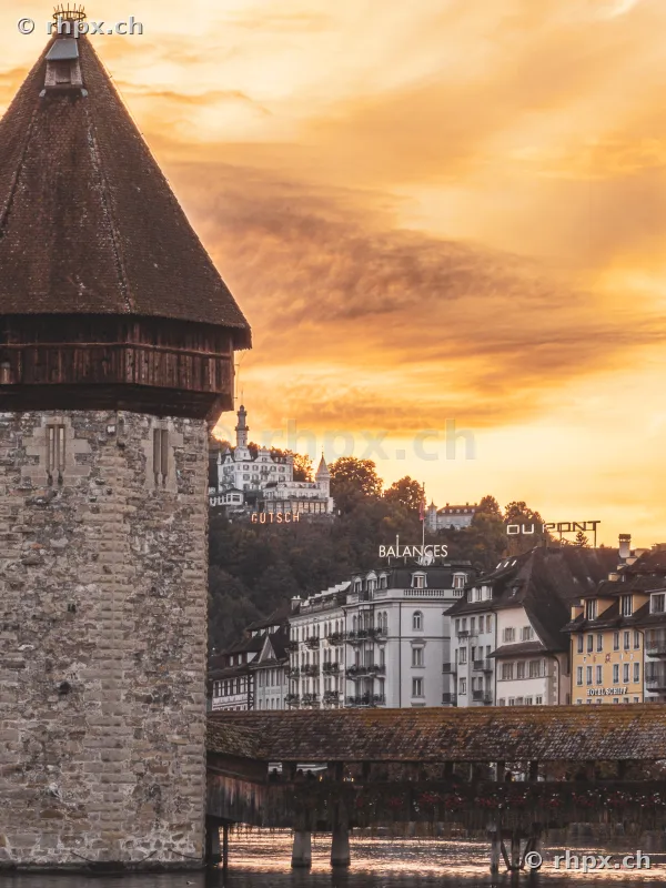 Water tower of the Chapel Bridge in Lucerne in front of buildings at sunset