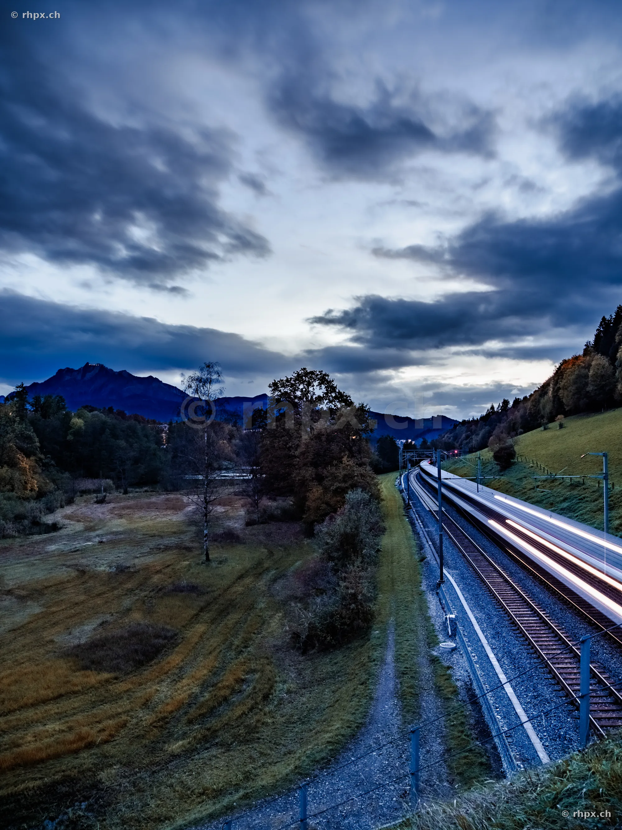 Passing train with motion blur in front of Mount Pilatus at dusk