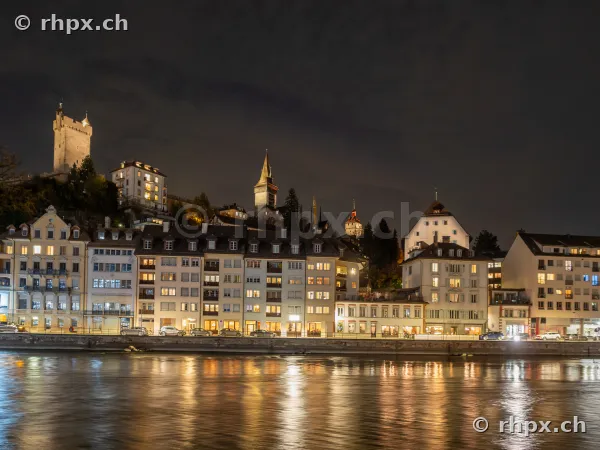 Beleuchtete Gebäudezeile an der Reuss in Luzern mit Museggmauer bei Nacht