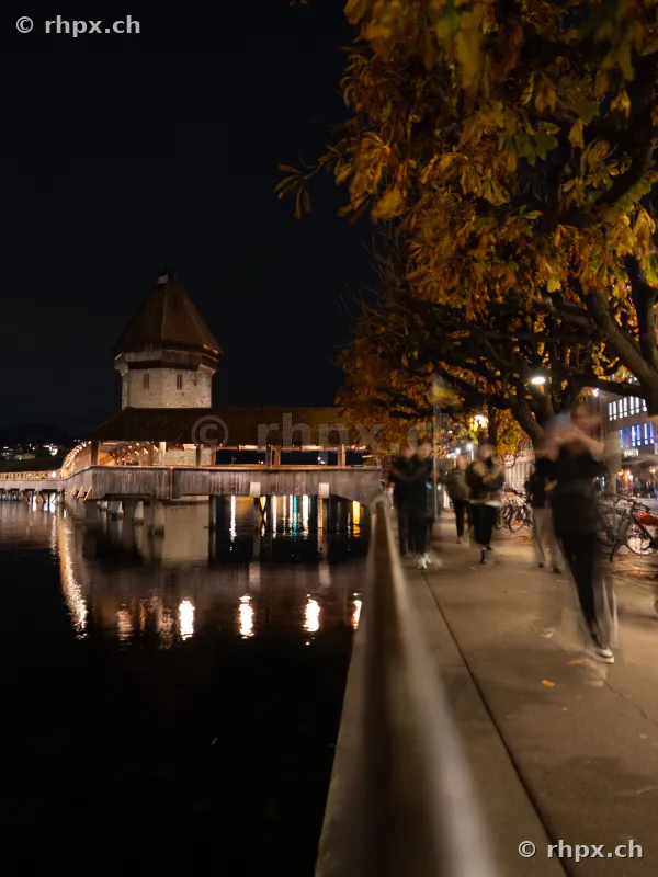Nächtlicher Blick auf die Kapellbrücke in Luzern mit herbstlichen Bäumen am Flussufer