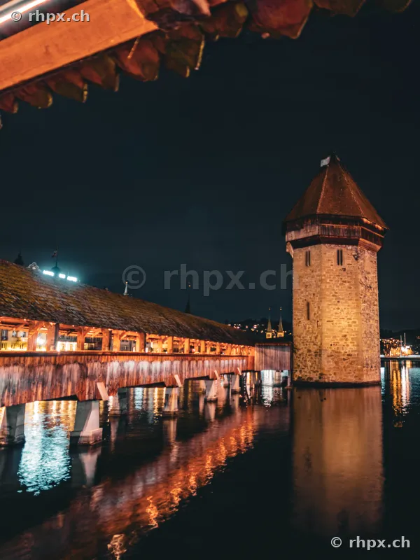 The illuminated Chapel Bridge and Water Tower in Lucerne at night.
