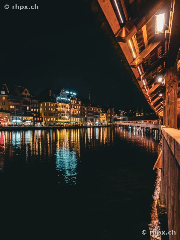 View from the Chapel Bridge over the nocturnal Reuss river towards the illuminated old town of Lucerne.