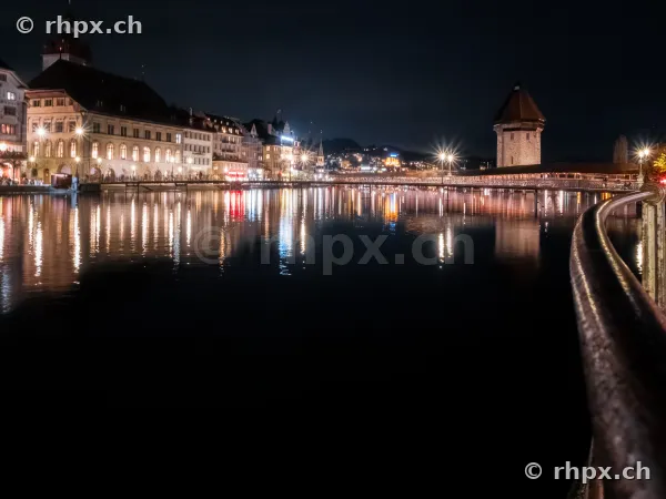 Night view of the illuminated Chapel Bridge and the old town of Lucerne along the riverbank.