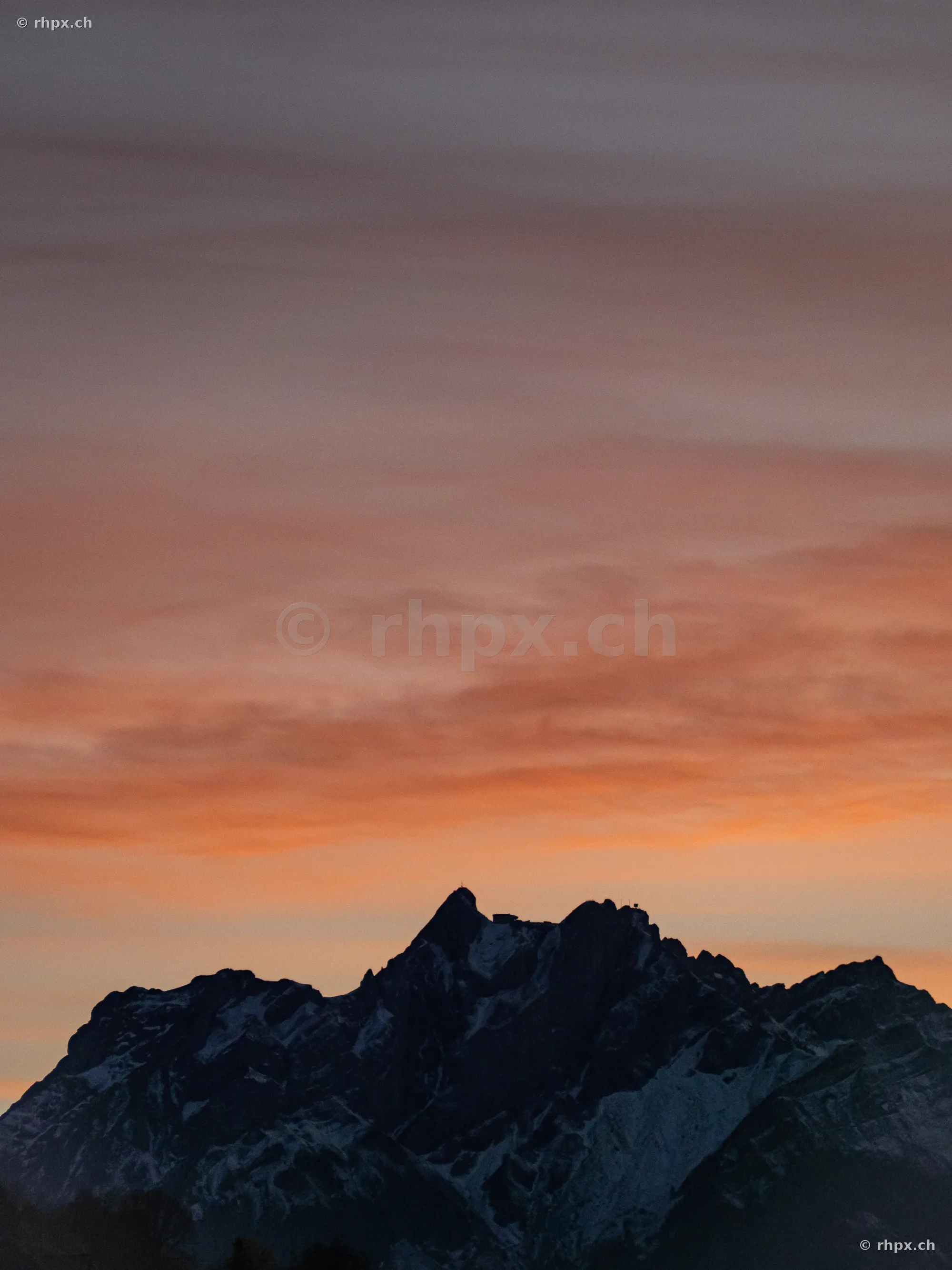 Silhouette of Mount Pilatus against an orange-colored evening sky