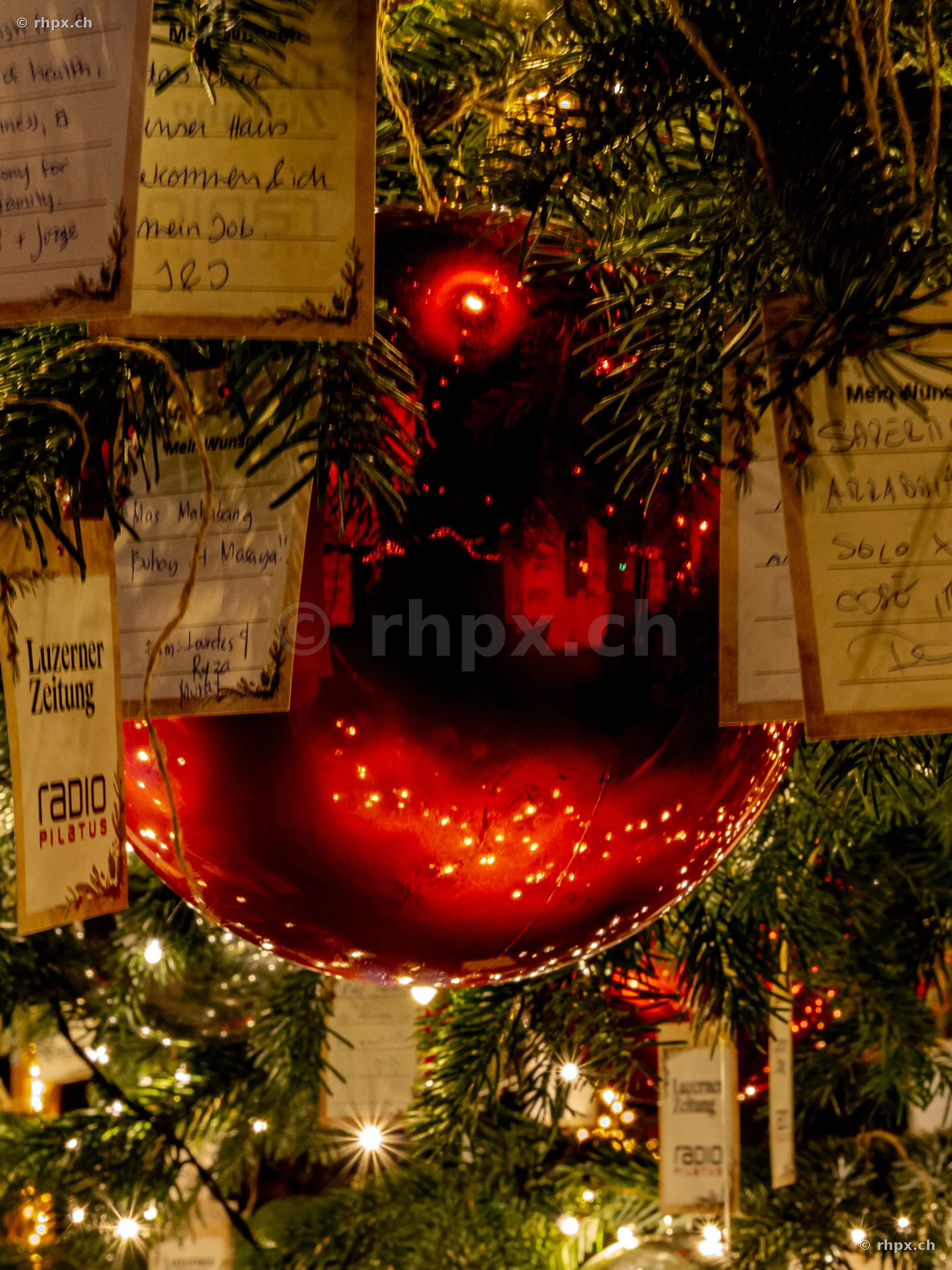 Rote Weihnachtskugel mit Wunschzetteln an einem beleuchteten Baum in Luzern