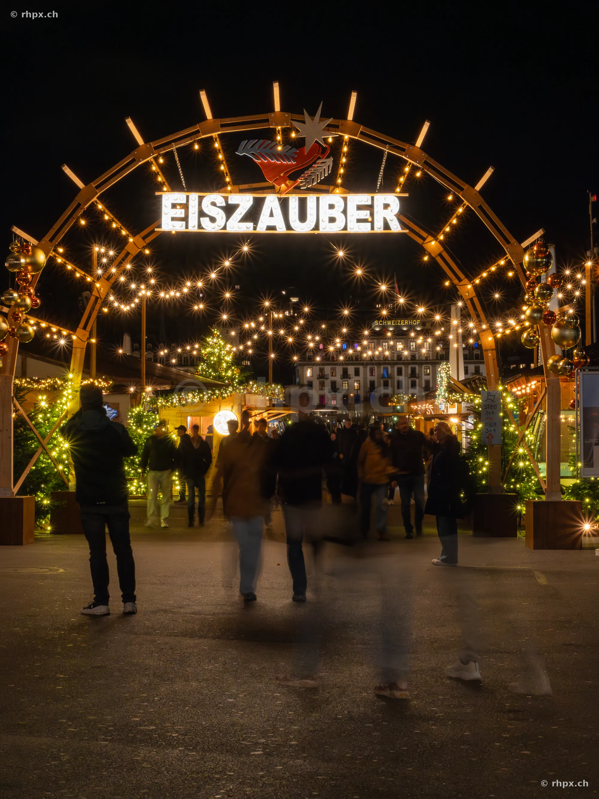 Illuminated entrance arch to the Ice Magic event in Lucerne with pedestrians at night