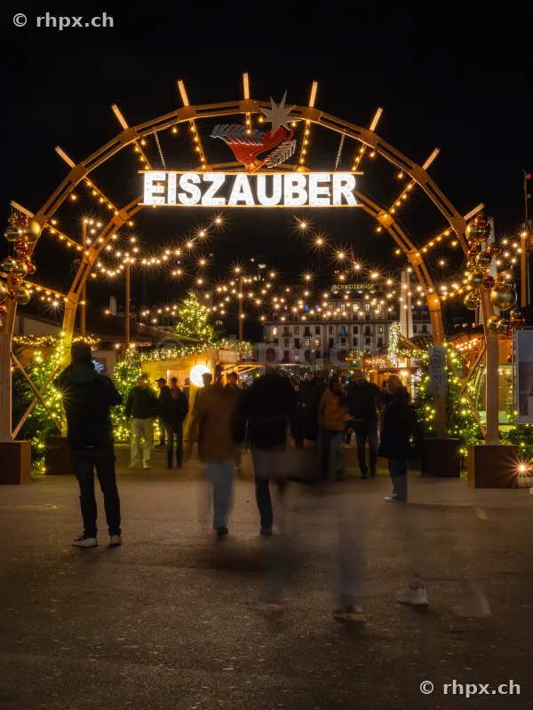 Illuminated entrance arch to the Ice Magic event in Lucerne with pedestrians at night