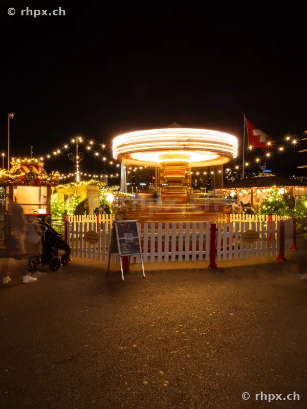 Weihnachtsmarkt mit beleuchtetem, rotierendem Karussell am Abend in Luzern