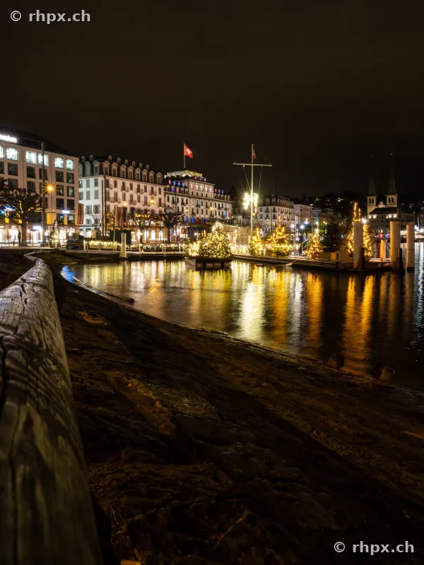 Weihnachtlich beleuchtetes Seeufer in Luzern bei Nacht mit Reflexionen im Wasser
