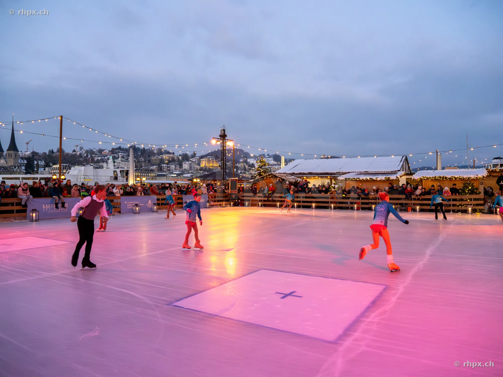 Menschen beim Eislaufen auf einer beleuchteten Bahn vor weihnachtlicher Kulisse am Vierwaldstättersee in Luzern.