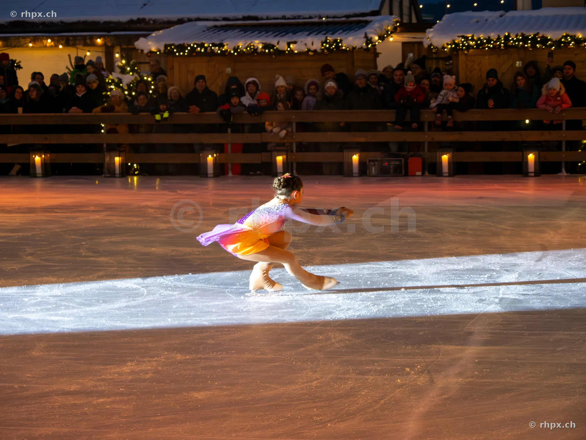 A figure skater in a colourful dress performing a pirouette on the ice rink at the Christmas market in Lucerne.