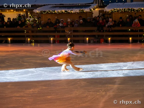 A figure skater in a colourful dress performing a pirouette on the ice rink at the Christmas market in Lucerne.