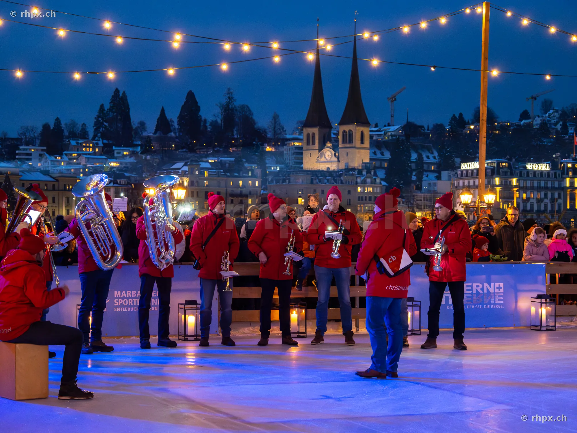 Musiker in roten Jacken spielen auf der Eislaufbahn in Luzern vor der Hofkirche