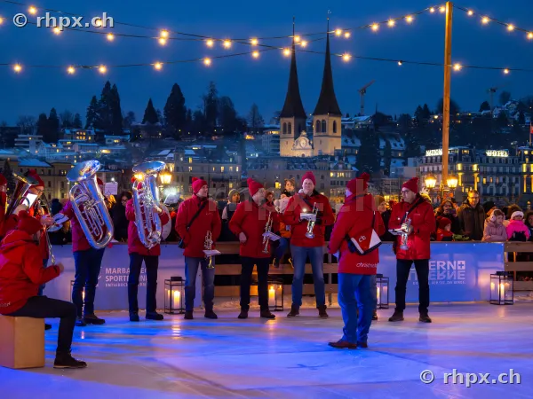 Musicians in red jackets playing on the ice rink in Lucerne in front of the Hofkirche