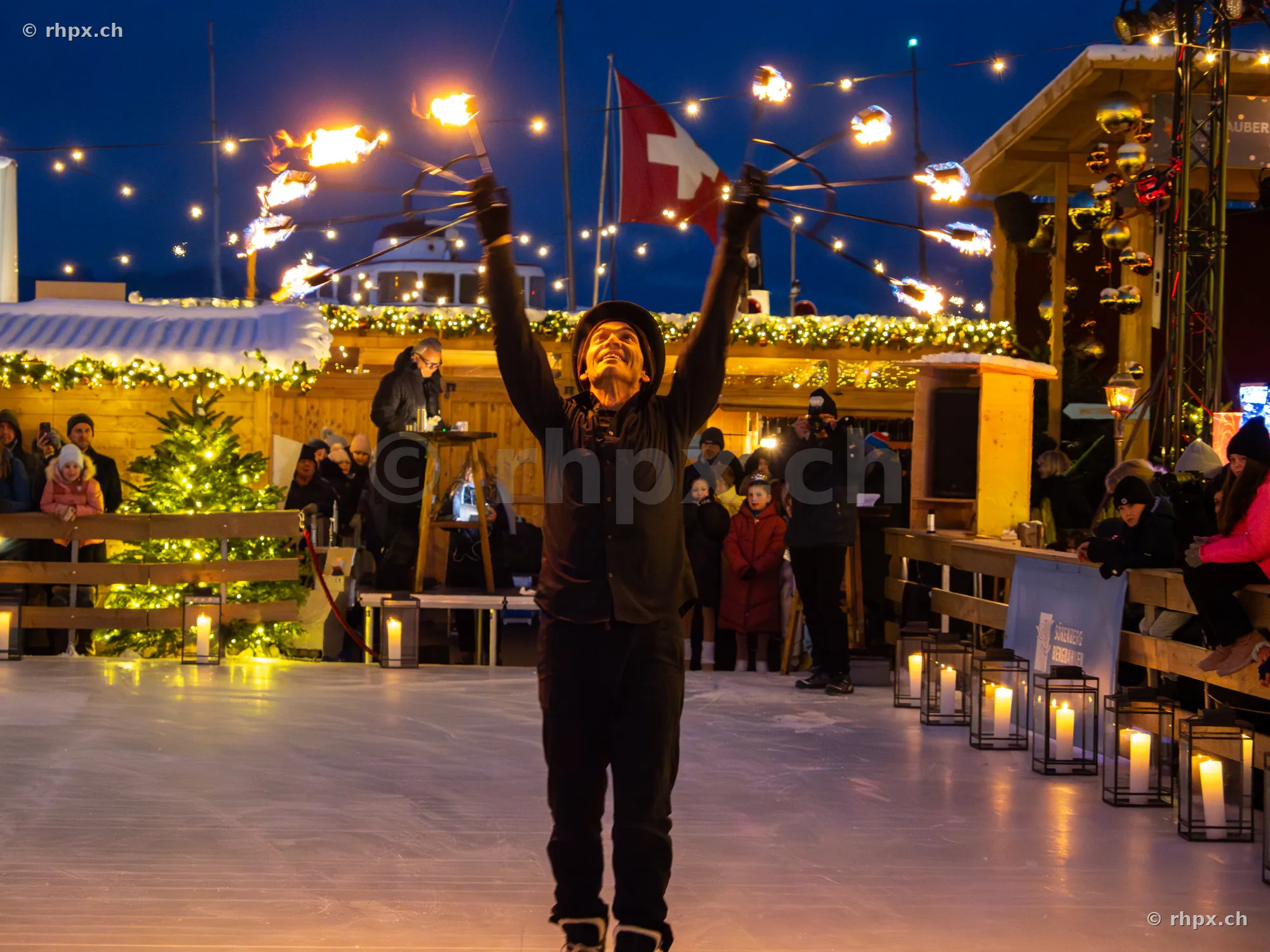 Ein Feuerkünstler mit brennenden Fackeln auf der Eislaufbahn in Luzern während der Weihnachtszeit.