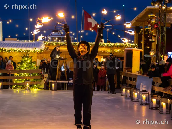 A fire performer with burning torches on the ice rink in Lucerne during the Christmas season.