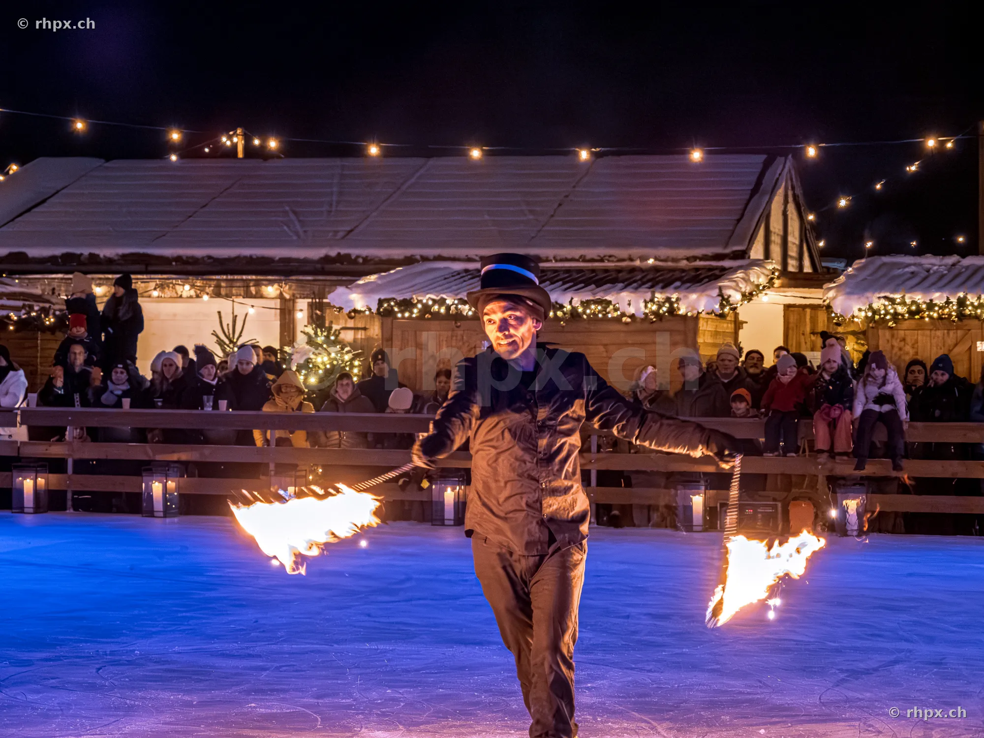 Ein Feuerkünstler mit Zylinder bei einer Performance auf dem Eisfeld in Luzern vor einem weihnachtlichen Marktstand