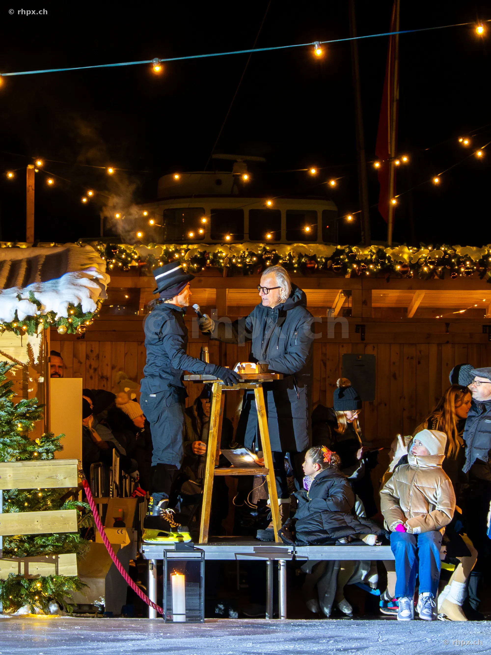 Two people on a stage in front of an audience at an ice rink in Lucerne during Christmas