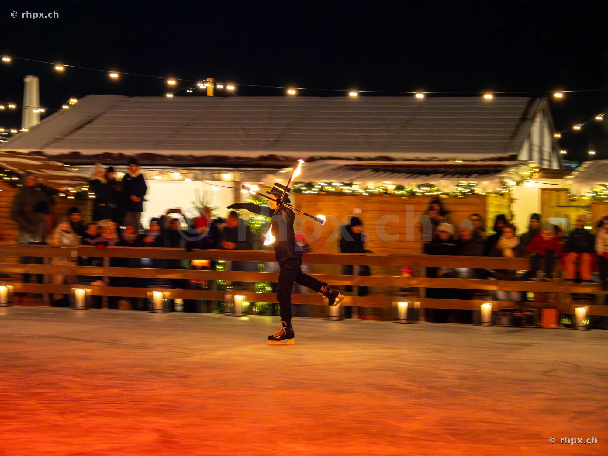 Person in Zylinder zeigt eine Feuershow auf der Eisbahn am Weihnachtsmarkt in Luzern
