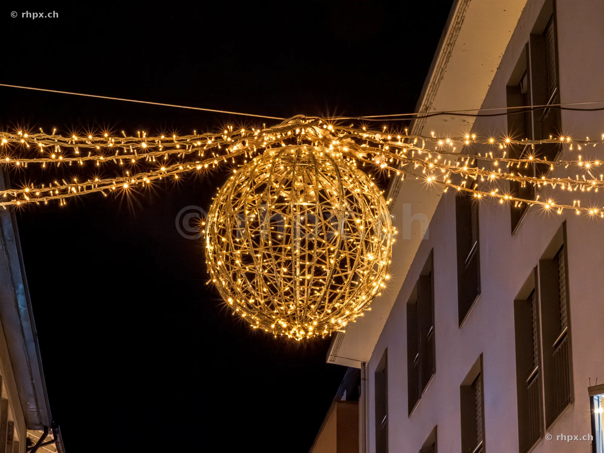 Eine grosse, leuchtende Kugel aus Lichterketten hängt als Weihnachtsdekoration über einer Strasse in Luzern bei Nacht.