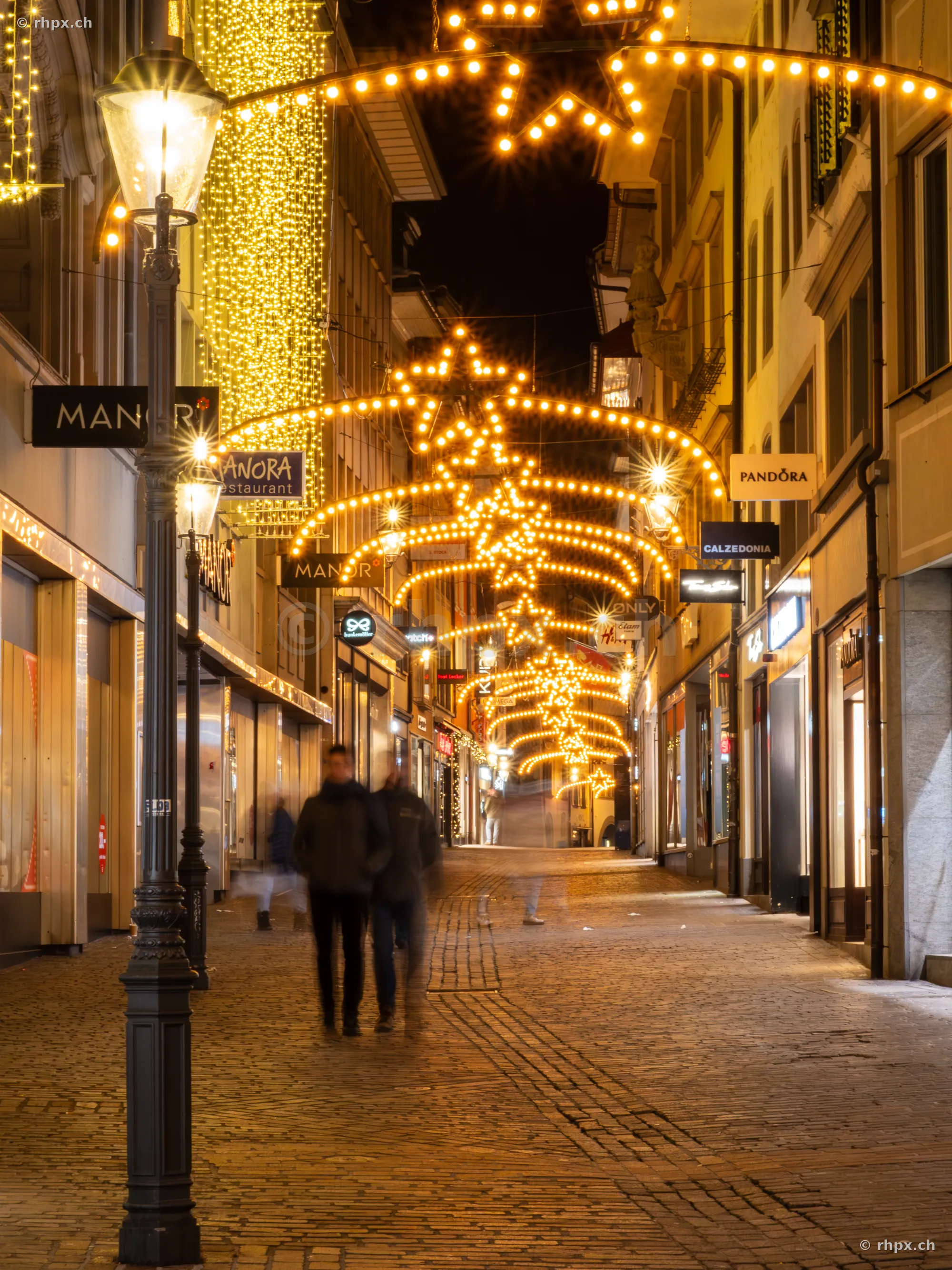Festliche Weihnachtsbeleuchtung in der nächtlichen Luzerner Altstadt mit Passanten auf dem Pflaster