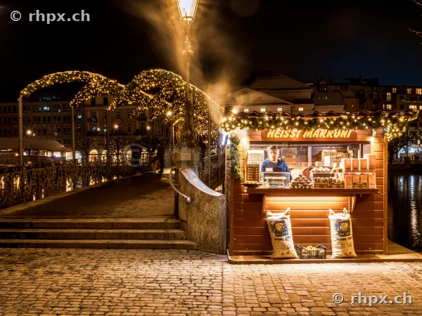 Illuminated chestnut stand by the bank of the Reuss river at night in Lucerne during Christmas