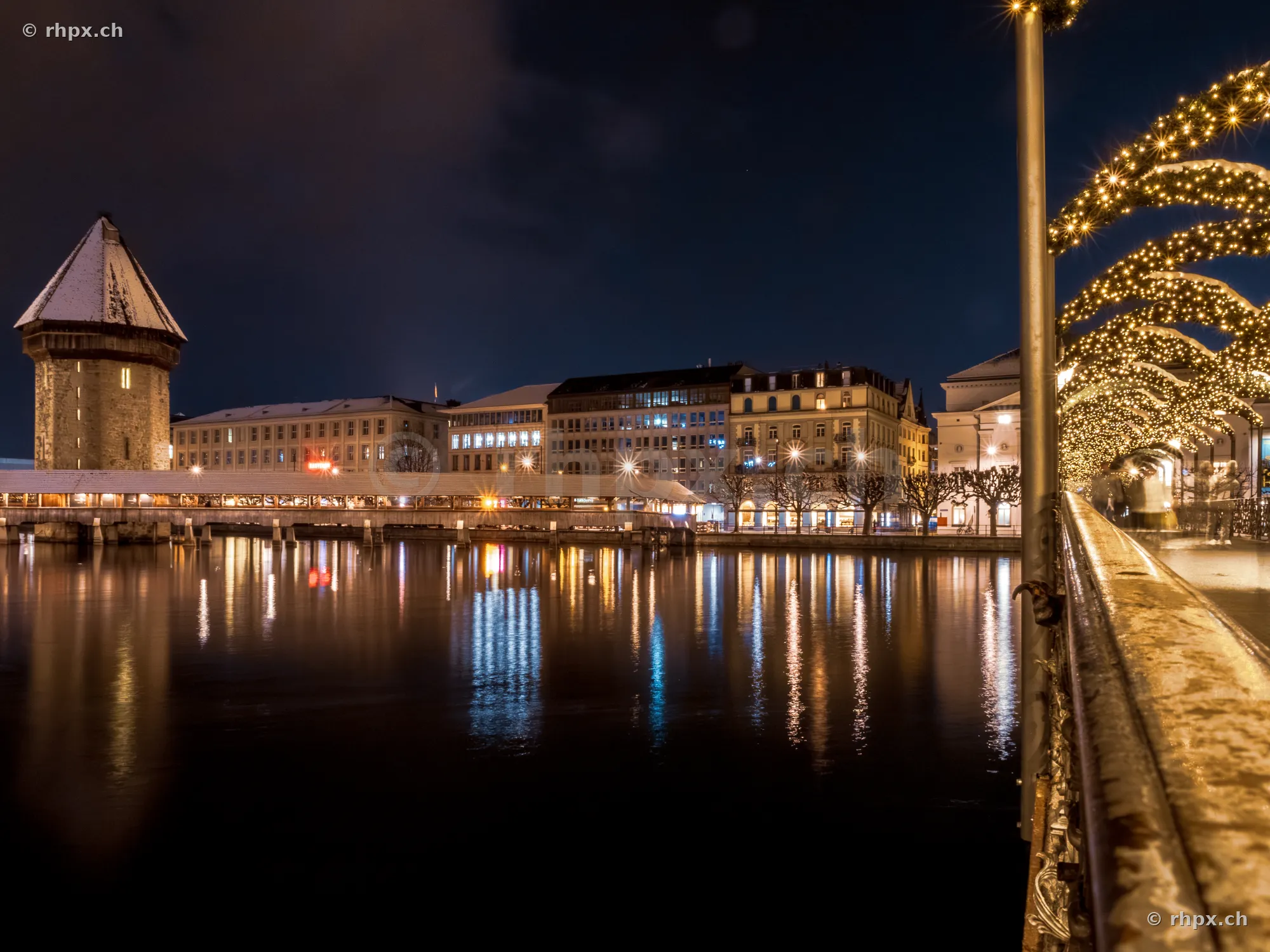 Night view of the snow-covered Chapel Bridge in Lucerne with festive Christmas lights in the foreground