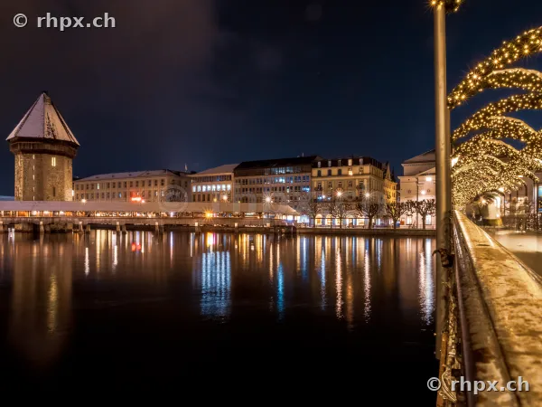 Night view of the snow-covered Chapel Bridge in Lucerne with festive Christmas lights in the foreground