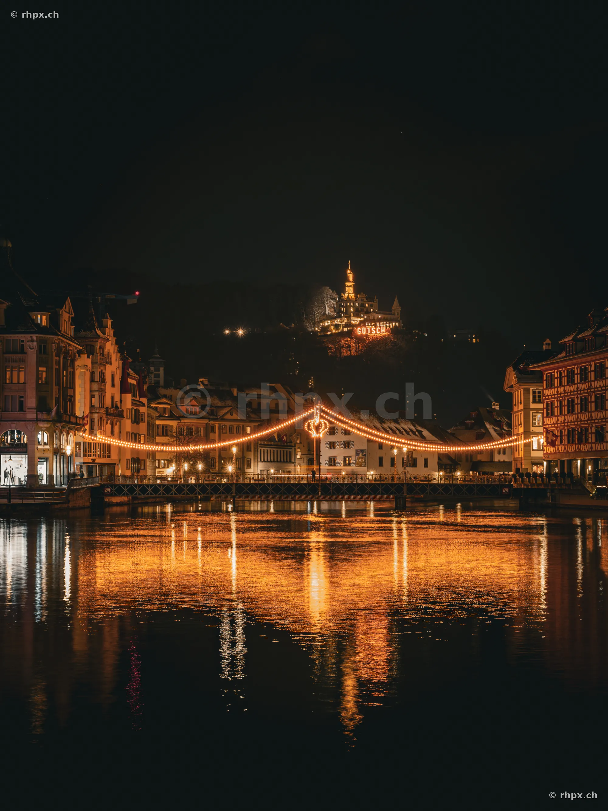 The festively illuminated Reuss bridge at night with the Gütsch in the background in Lucerne