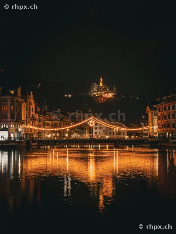 The festively illuminated Reuss bridge at night with the Gütsch in the background in Lucerne