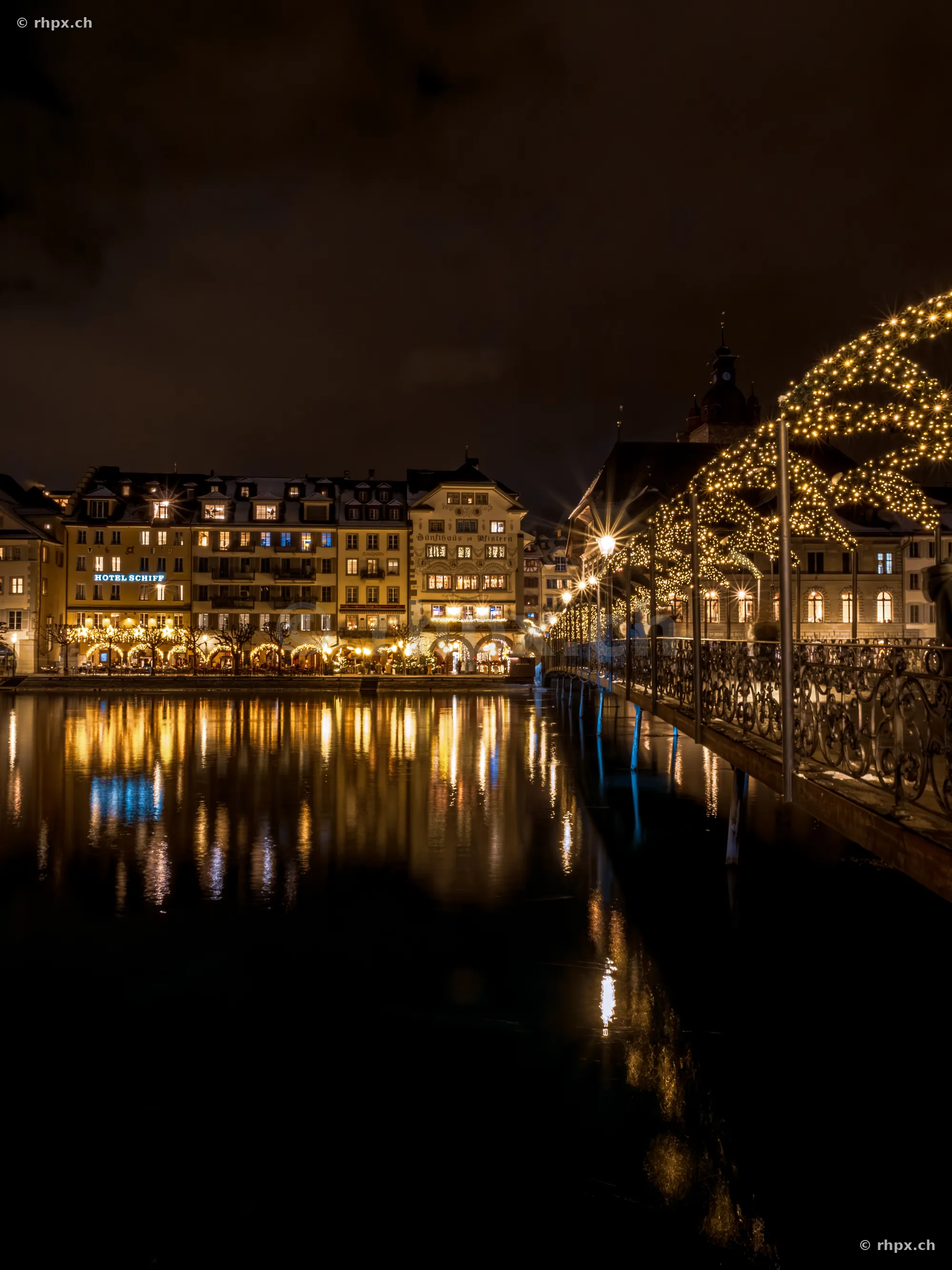 Nighttime riverside promenade in Lucerne with Christmas lights on a pedestrian bridge