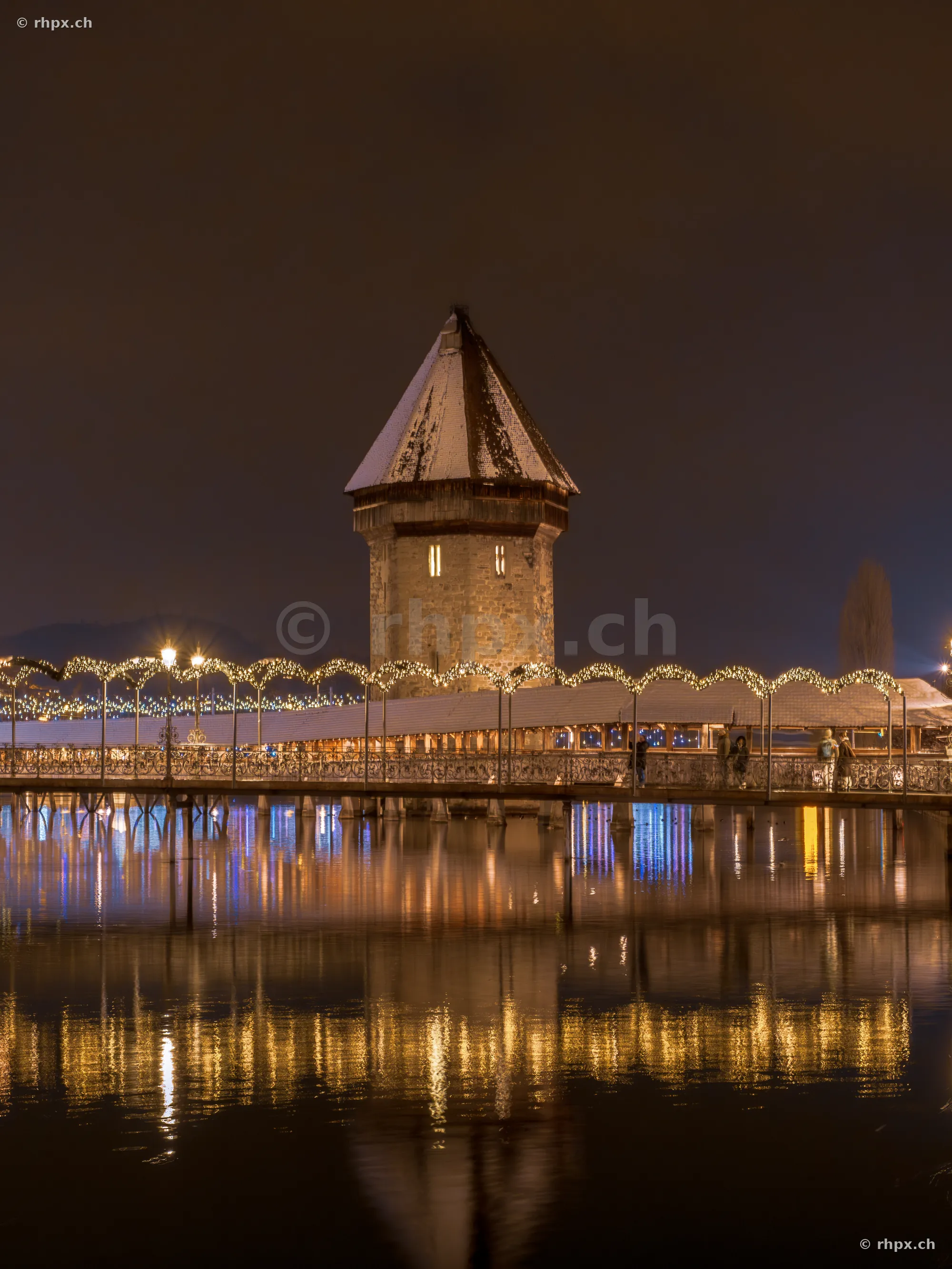 Night view of the snow-covered Chapel Bridge with Christmas lighting in Lucerne