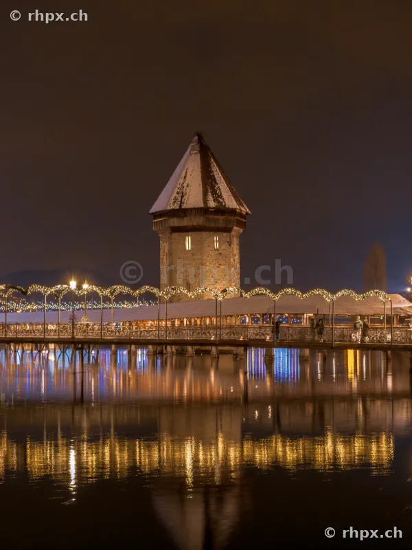 Night view of the snow-covered Chapel Bridge with Christmas lighting in Lucerne