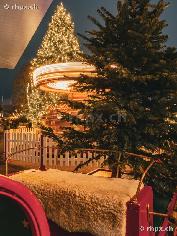 Weihnachtlich beleuchtetes Karussell und Tannenbaum vor einem Schlitten am Luzerner Seebecken bei Nacht