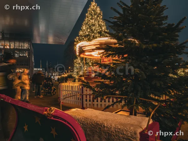 Christmas market in front of the KKL Lucerne with an illuminated carousel and Christmas tree at night