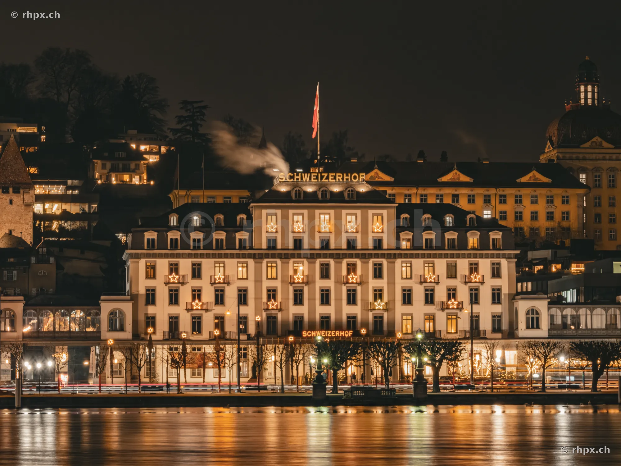 Das beleuchtete Hotel Schweizerhof in Luzern bei Nacht mit weihnachtlichem Sternenschmuck.