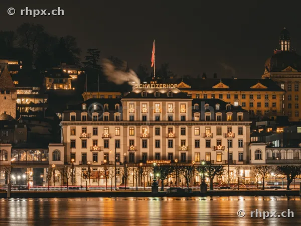 The illuminated Hotel Schweizerhof in Lucerne at night with Christmas star decorations.