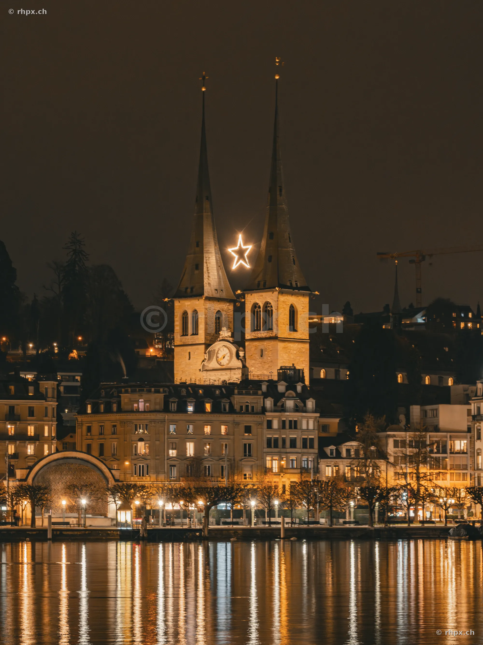 Illuminated towers of the Hofkirche in Lucerne with a glowing star between the spires at night.